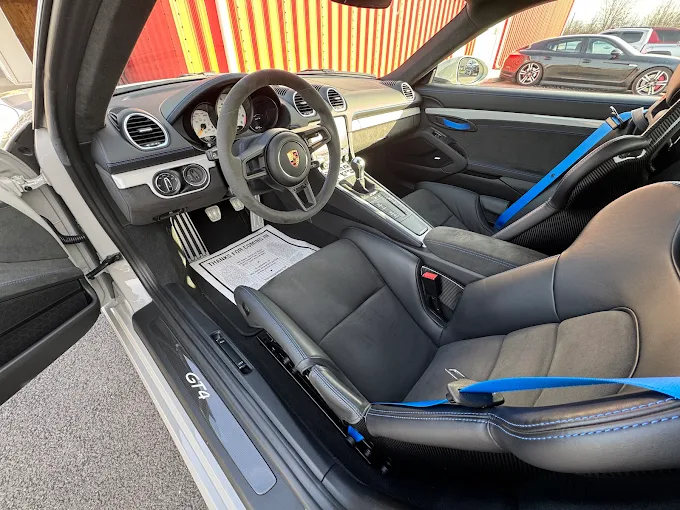 Interior of a white Porsche 718 Cayman GT4 with blue seat belts