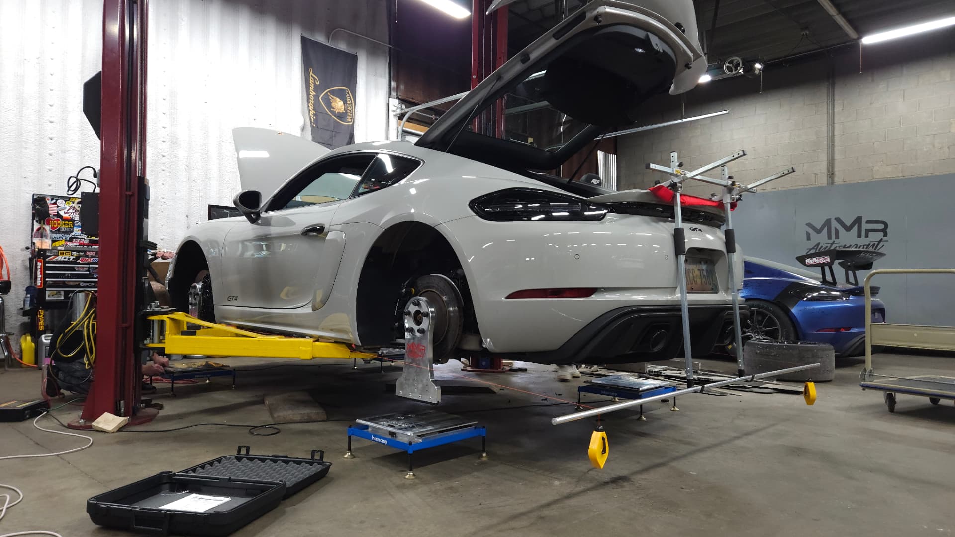 White Porsche 718 Cayman GT4 on a lift during a corner-balance and alignment setup