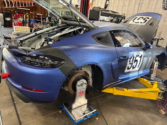 Blue number 951 Porsche Cayman race car on stands in the MMr Autosport shop