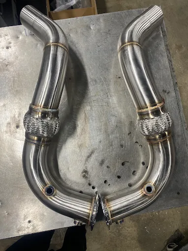 Custom stainless exhaust pipes laid out on a workbench