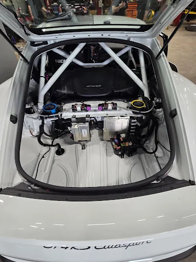 Open rear bay of a white Porsche GT4 RS Clubsport showing the roll cage and electronics