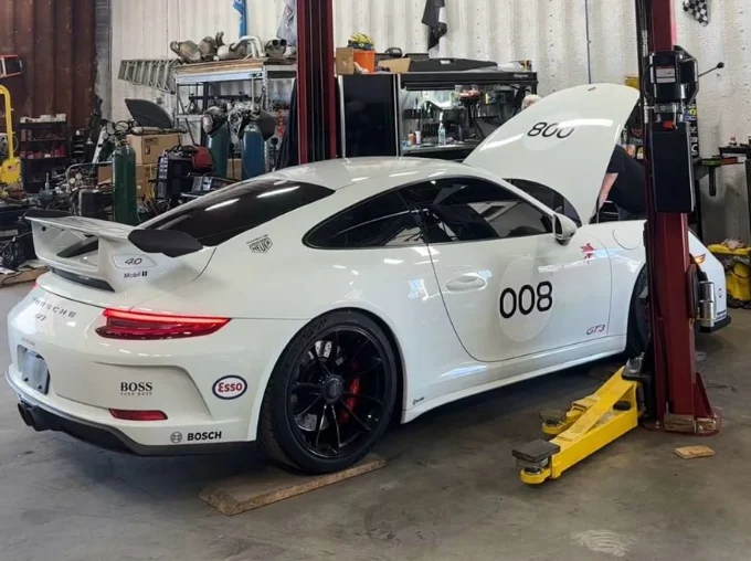 White Porsche 911 GT3 numbered 008 on a lift with its hood open