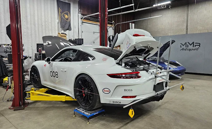 Rear view of the white Porsche 911 GT3 numbered 008 on a lift in the shop